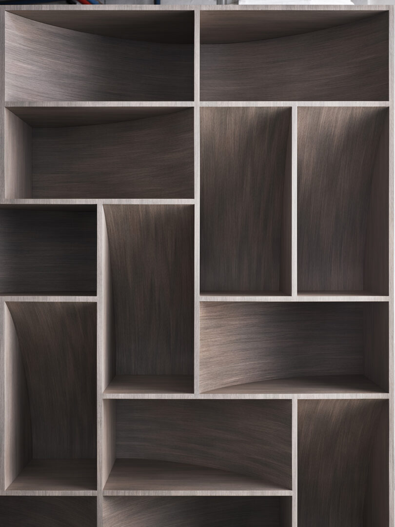 Empty wooden bookshelf with multiple asymmetrical rectangular compartments arranged in a modern, geometric pattern.