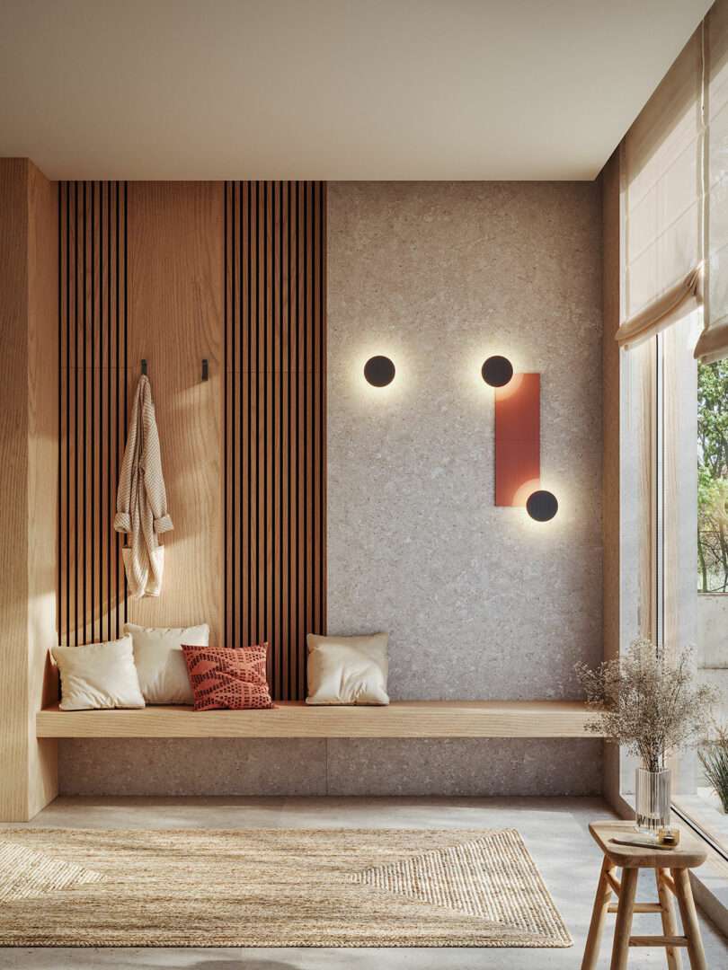 A modern entryway with a built-in wooden bench, beige and red cushions, wall hooks with hanging items, minimalist wall lights, and a window with natural light.