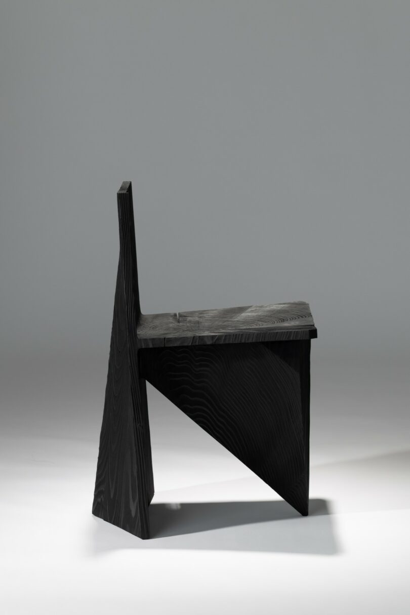 A modern, geometric wooden chair with a black finish and angular design, photographed against a plain light gray background