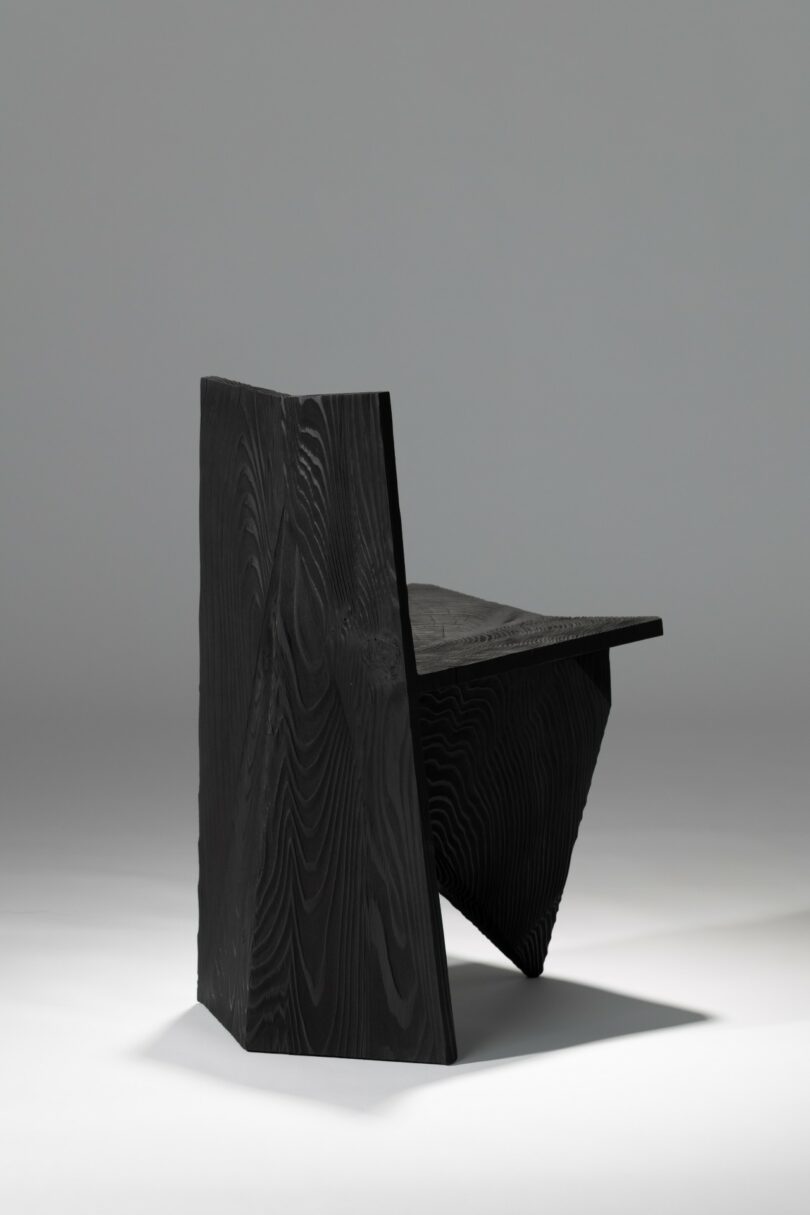 A black, angular chair with geometric shapes and sharp edges, photographed against a plain, light gray background