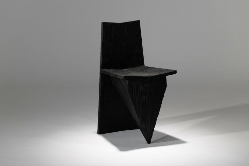 A black, angular chair with geometric shapes and sharp edges, photographed against a plain, light gray background