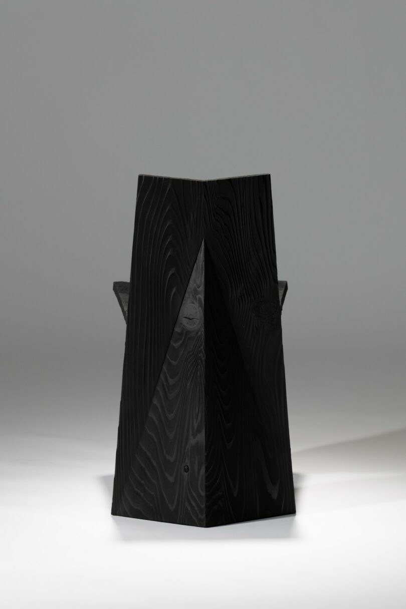 A black, angular chair with geometric shapes and sharp edges, photographed against a plain, light gray background