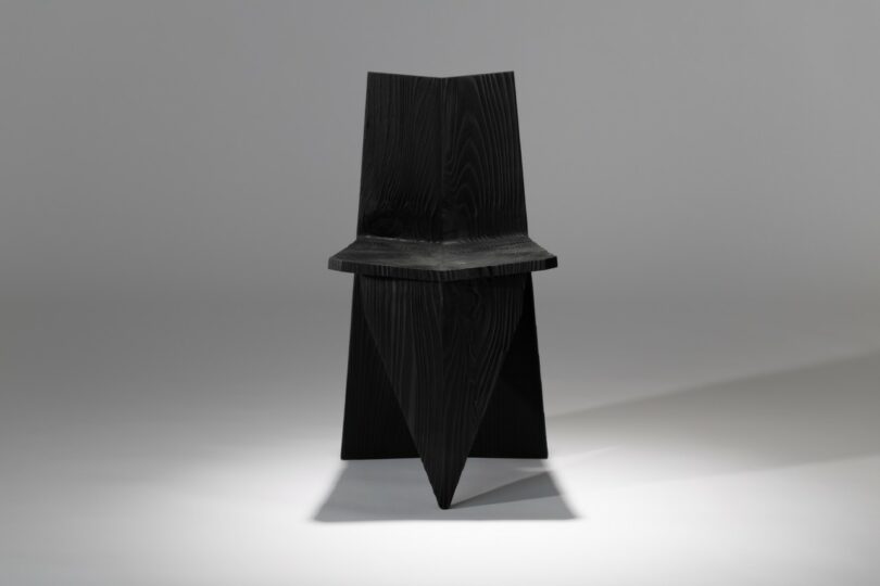A black, angular chair with geometric shapes and sharp edges, photographed against a plain, light gray background