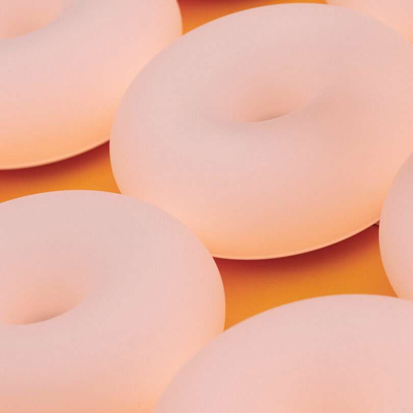 Close-up of several pastel pink, smooth, doughnut-shaped objects arranged on a flat, orange surface.