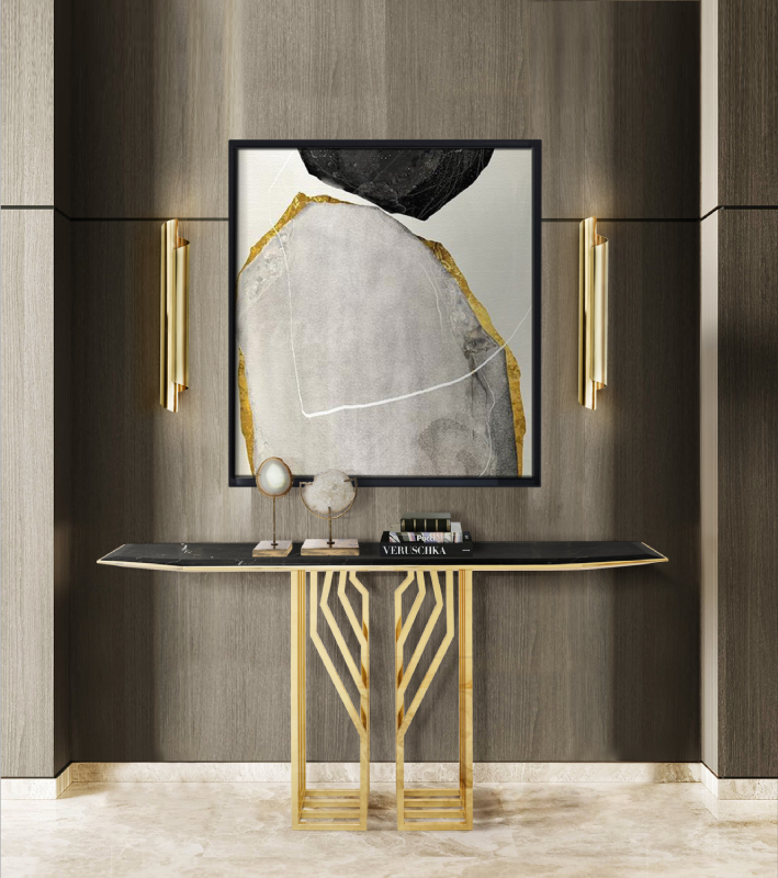 Luxury entryway featuring a black marble-top console table with geometric gold legs, a large-scale gray and gold abstract painting, and two vertical brass wall sconces against dark wood paneling.