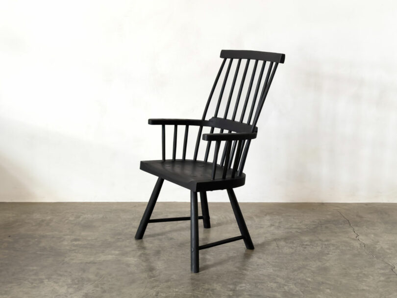 A black wooden Windsor chair with vertical spindles, armrests, and angled legs sits on a concrete floor against a plain white wall—a timeless pick for any Friday Five design roundup.