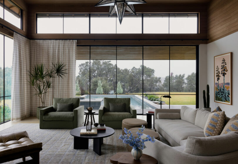 Modern living room with large windows overlooking a pool and trees, featuring neutral-toned furniture, indoor plants, contemporary decor, and perfect for relaxing after a busy Friday 5.