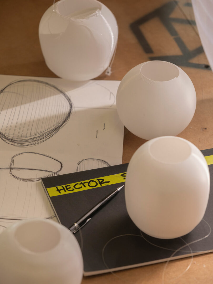 Four white spherical objects are placed on a table with sketchpads showing sphere drawings, a pen, and a folder labeled 