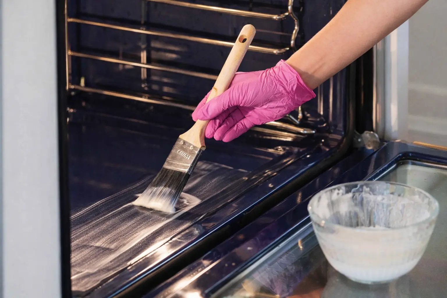 An image of a person cleaning the insides of their oven with a baking soda and vinegar mixture. They are brushing it onto the oven surface.