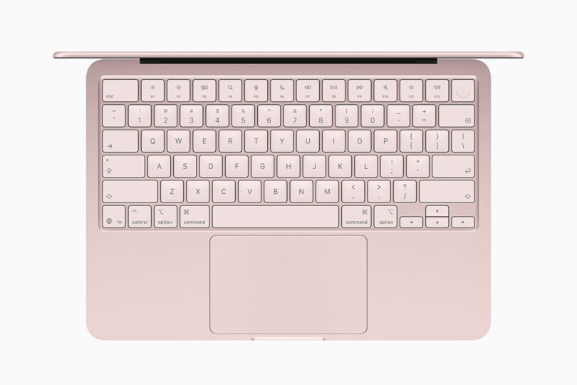 A pink Apple laptop viewed from above, showing the keyboard, trackpad, and part of the screen hinge.