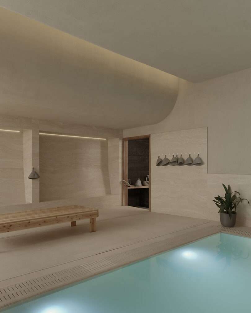 Minimalist indoor pool area with soft beige walls, a wooden bench, wall hooks with towels, a potted plant, and a door leading to a darker room.