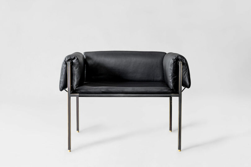A modern black leather chair by ATRA with metal legs and draped armrests, set against a plain light gray background.