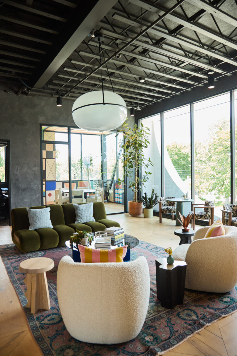 Modern Powell office lounge with large windows, green and white seating, a patterned rug, potted plants, and a circular overhead light fixture.