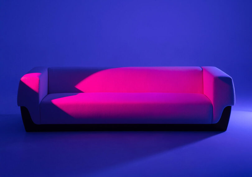 A modern Holly Hunt sofa illuminated by pink and blue lights against a blue background.