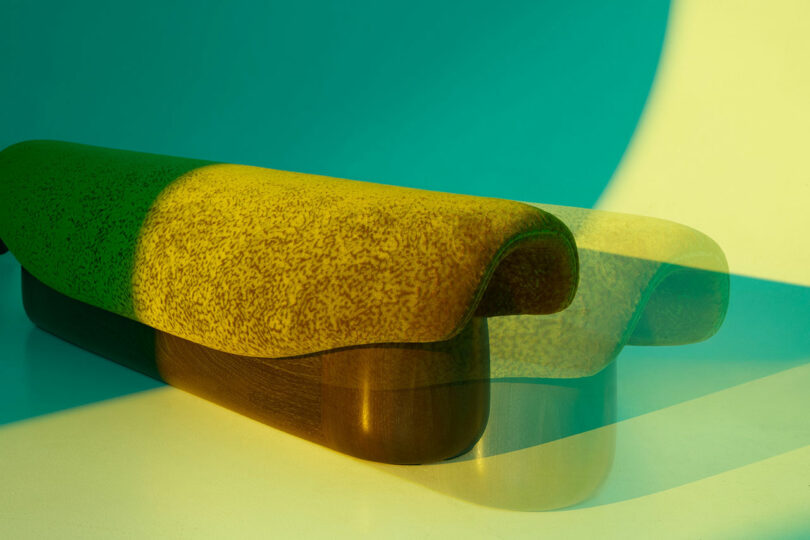 A contemporary Holly Hunt bench with a speckled yellow cushion and wooden base, photographed with dramatic lighting and a double exposure effect casting overlapping shadows.