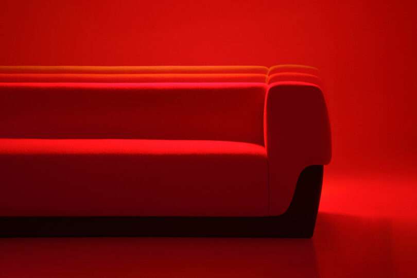 Red modern sofa from Holly Hunt against a red background, photographed from the side with dramatic lighting that creates distinct shadows and highlights.