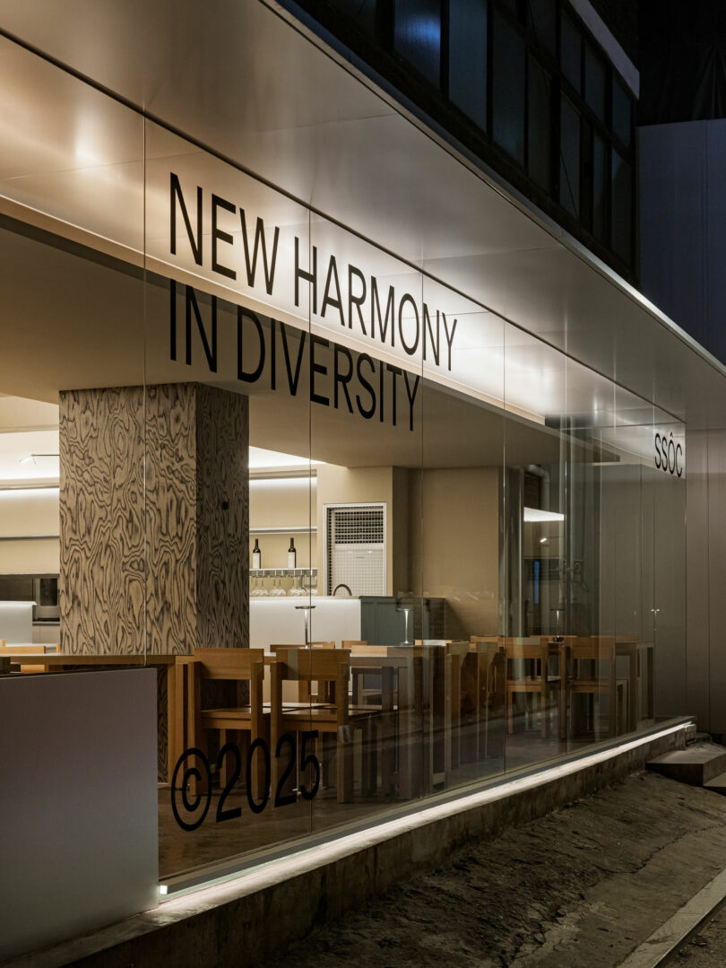 Modern interior of a building with wooden tables and chairs, seen through glass walls displaying the text 