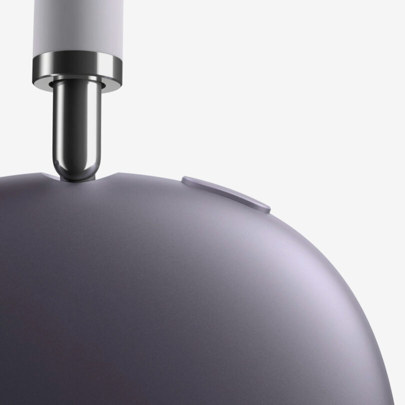 Close-up of a metallic device with a rounded surface, a button, and a cylindrical connector inserted into a port at the top—resembling the refined design details found in AirPods Max 2.