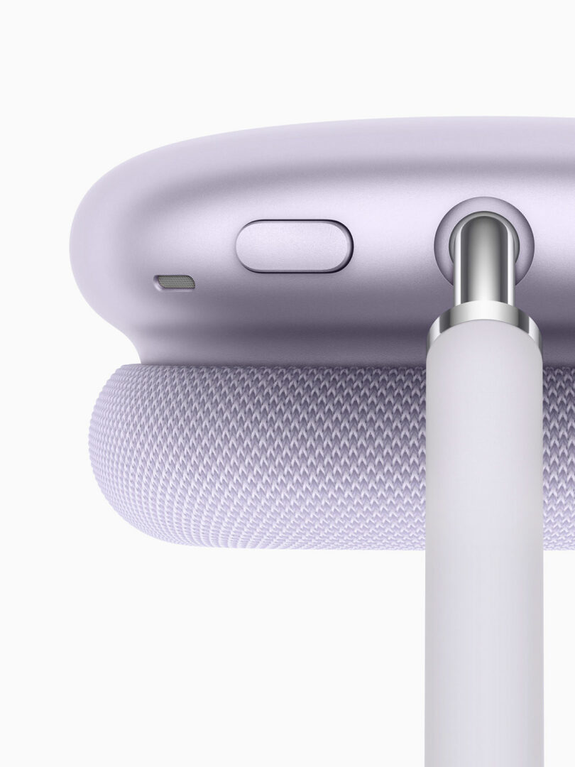 Close-up of lavender-colored AirPods Max 2 over-ear headphones with a charging cable plugged in and a control button visible.