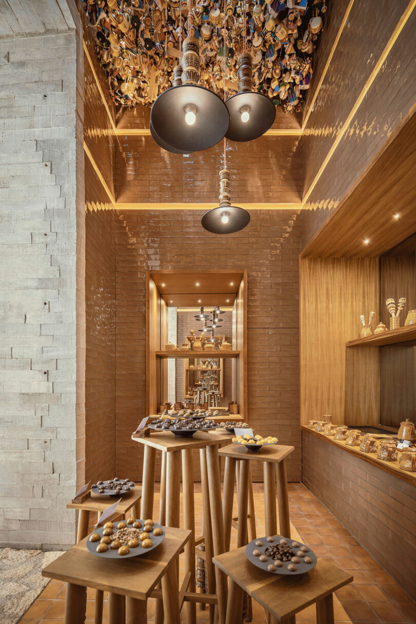 A modern confectionery shop with wooden tables displaying assorted chocolates, warm lighting, and decorative ceiling elements. Shelves on the right hold jars and more sweets.