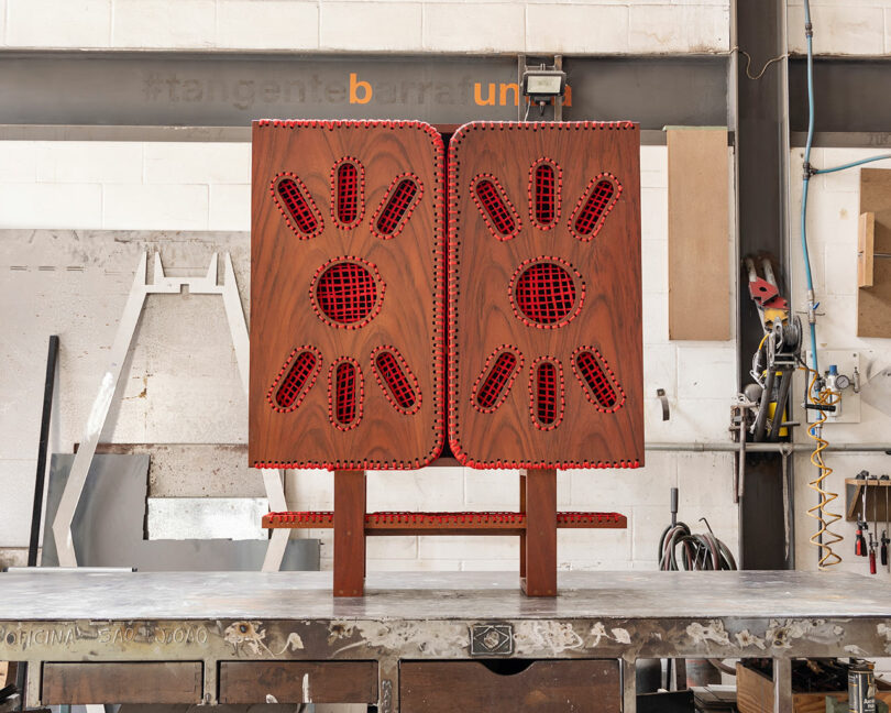 A wooden cabinet with red accents and geometric cutouts stands on a metal workbench in an industrial workshop.