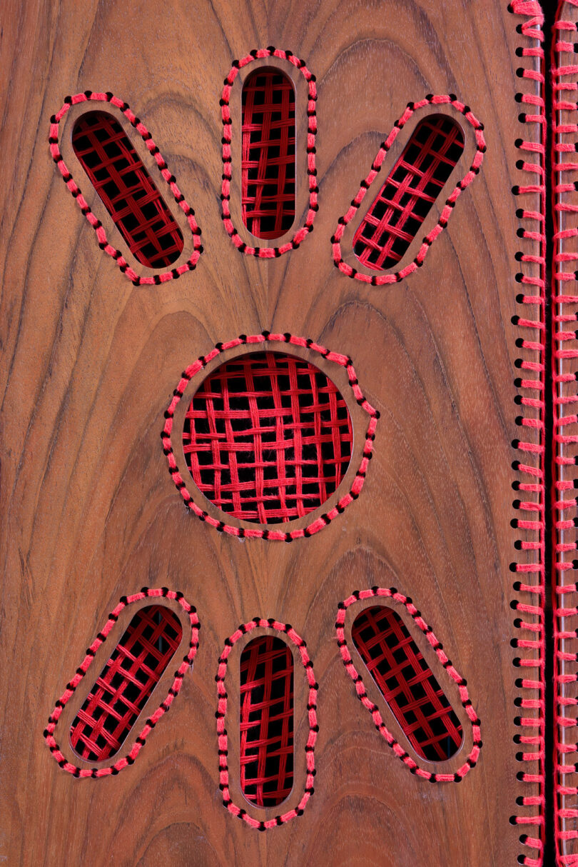 A wooden surface featuring several oval and one round cutouts, all filled with red latticework and bordered with red stitching.
