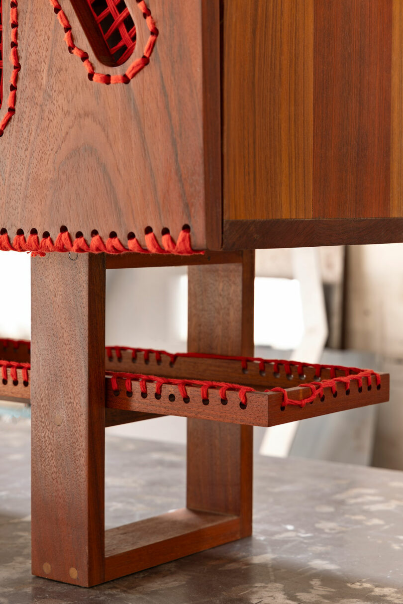 Close-up of a wooden piece of furniture featuring red cord stitching along the edges and a geometric leg design.