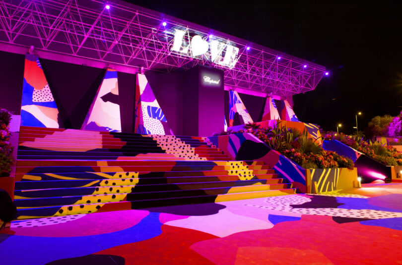 A colorful, geometric-painted staircase and platform are illuminated by purple lights at night, with a glowing 