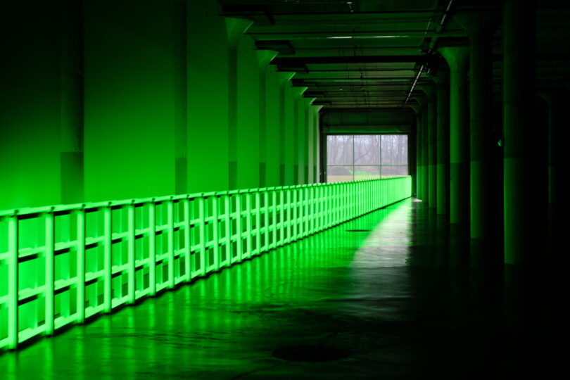 A long corridor with a white railing is illuminated by green light, leading to a bright, open exit at the far end—an inviting scene from Friday 5.