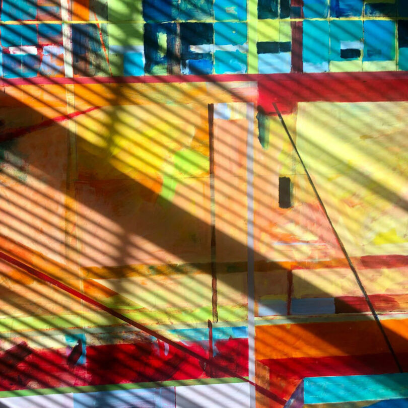 Abstract geometric painting by Barry Ginder features colorful rectangles and lines, overlaid with diagonal shadows from window blinds.