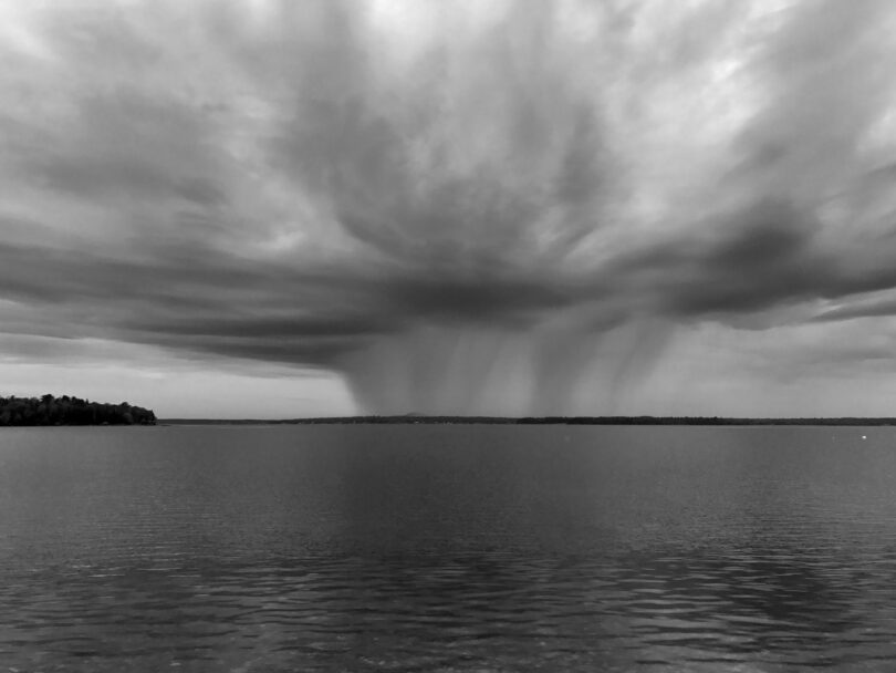 A rainstorm is visible in the distance over a calm body of water under a cloudy sky, creating a perfect scene for Friday 5.