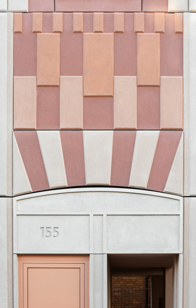 Geometric facade with pink and beige panels above an arched doorway, featuring the number 155 and a partially visible entrance.