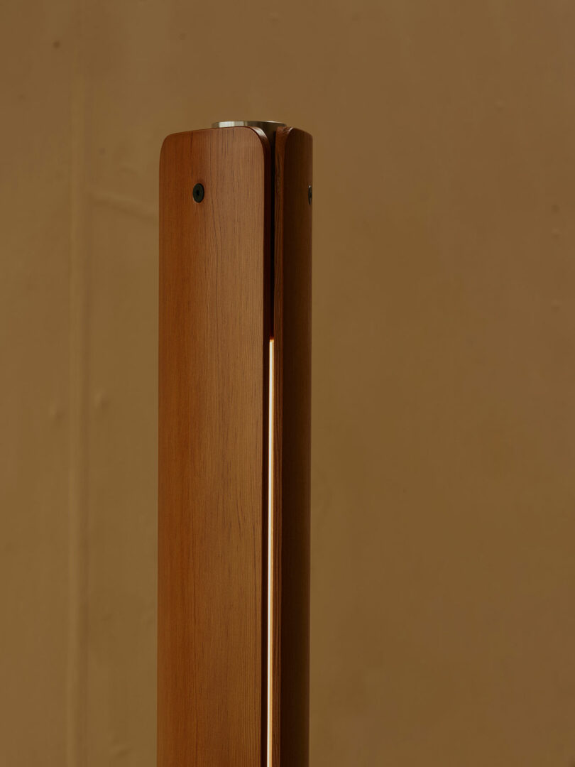 A close-up of a vertical wooden post with a narrow, vertical light strip and two visible screws against a plain brown background.
