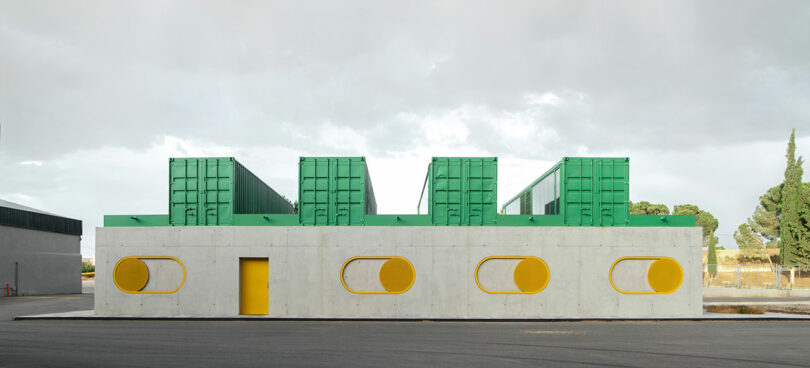 A modern building with a white concrete facade, yellow circular windows and door, and green rectangular structures on the roof, designed by Impepinable Studio.