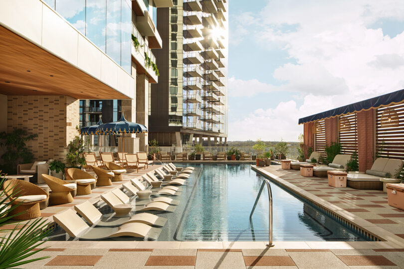 Outdoor pool area at Roost Rainey, a modern apartment complex with lounge chairs, umbrellas, and seating areas, surrounded by tall buildings and lush greenery.