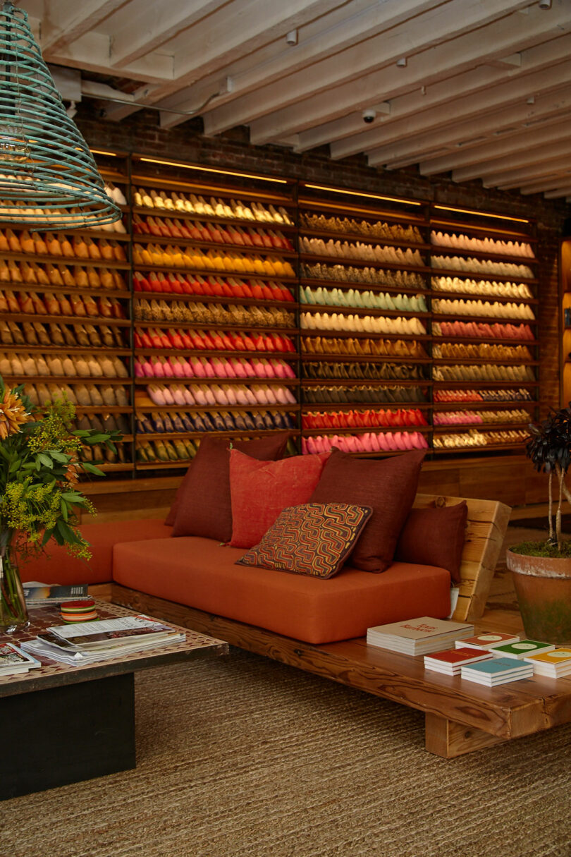 A cozy seating area with orange and red cushions is in front of a wall displaying shelves filled with neatly arranged colorful shoe pairs.