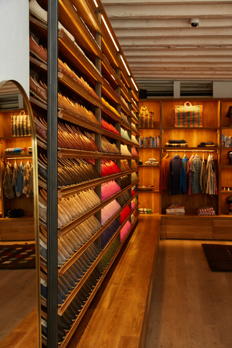 A clothing store with wooden shelves displaying neatly arranged colorful ties in the foreground and folded shirts and jackets in the background.