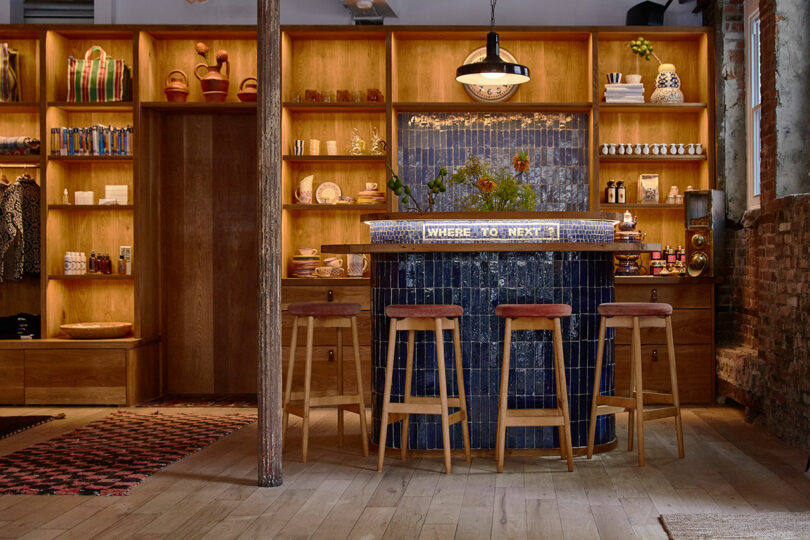 A cozy bar area with four wooden stools, a tiled counter, shelves displaying various items, and a 