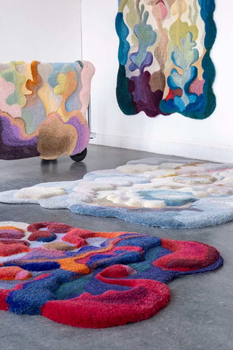 Colorful, abstract, textured rugs and furniture with organic shapes bring a shimmering real touch to a gray floor and white wall in this modern interior setting.