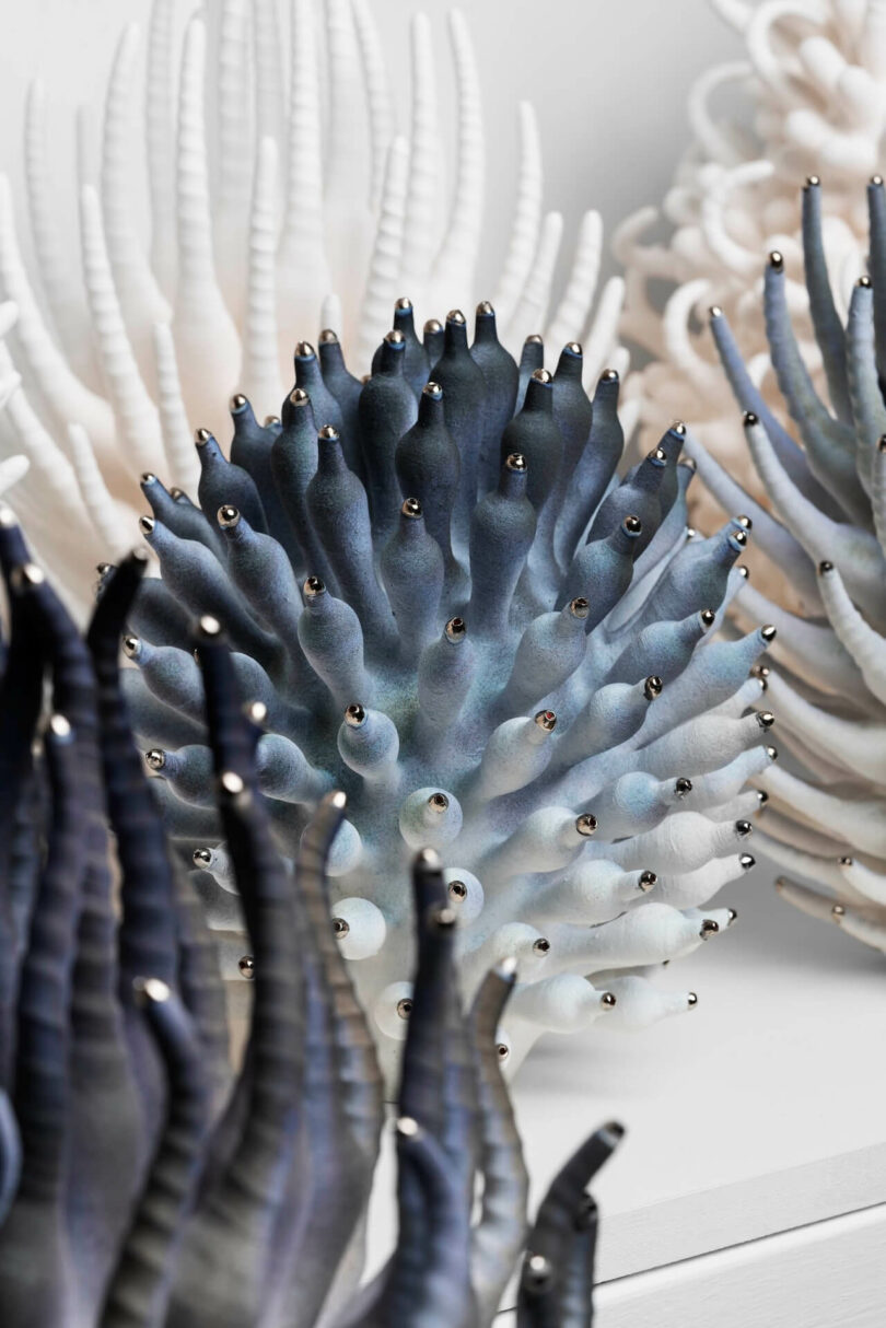 A close-up of sculpted objects resembling shimmering real sea anemones, with pointed, textured shapes in shades of blue, white, and black, each tip capped with a small metallic bead.