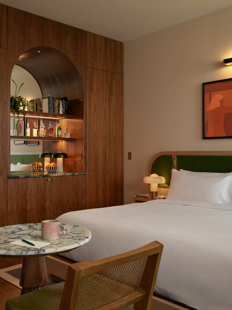 A hotel room at Municipal Grand features a neatly made bed, marble-topped table, chair, wood-paneled wall, built-in bar nook, and striking modern artwork on the wall.