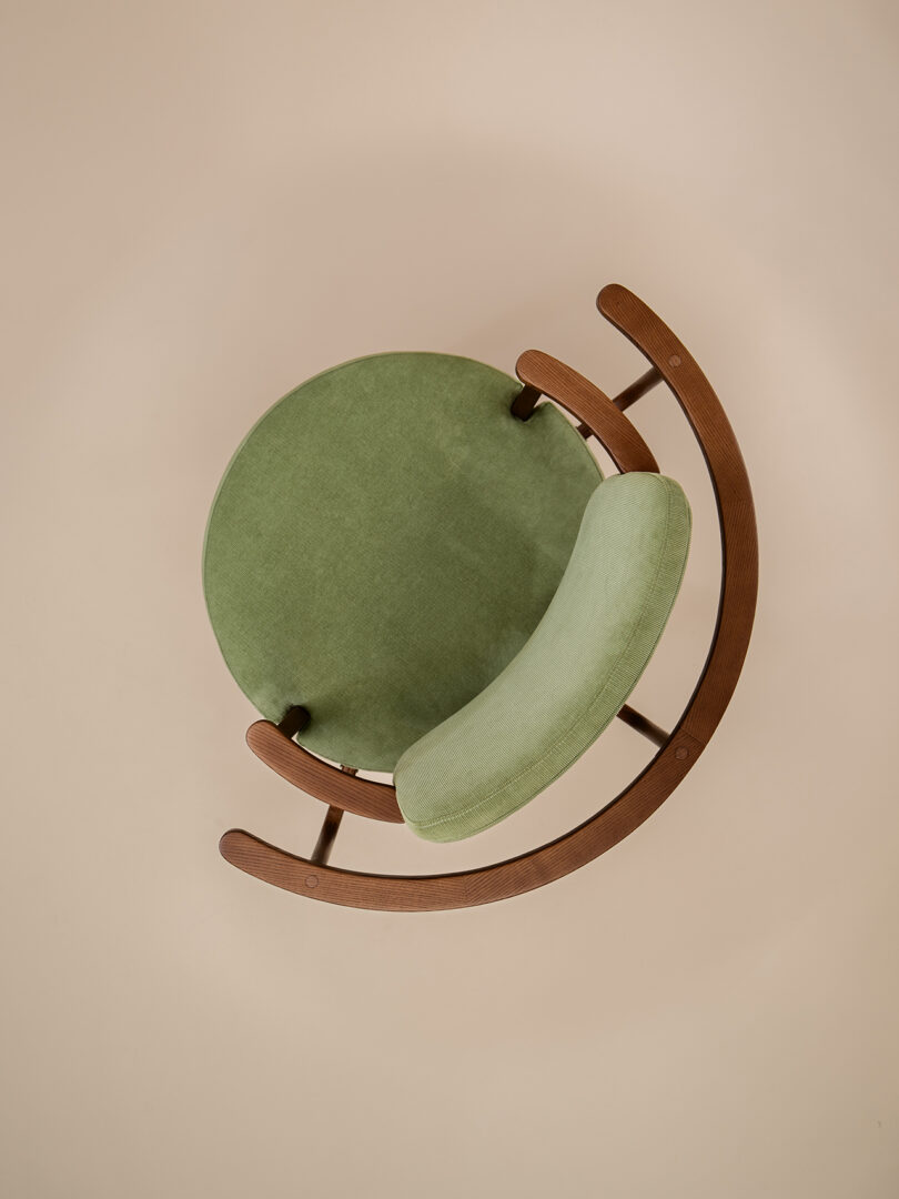 Overhead view of a modern chair with a circular green seat and curved wooden frame on a beige background.