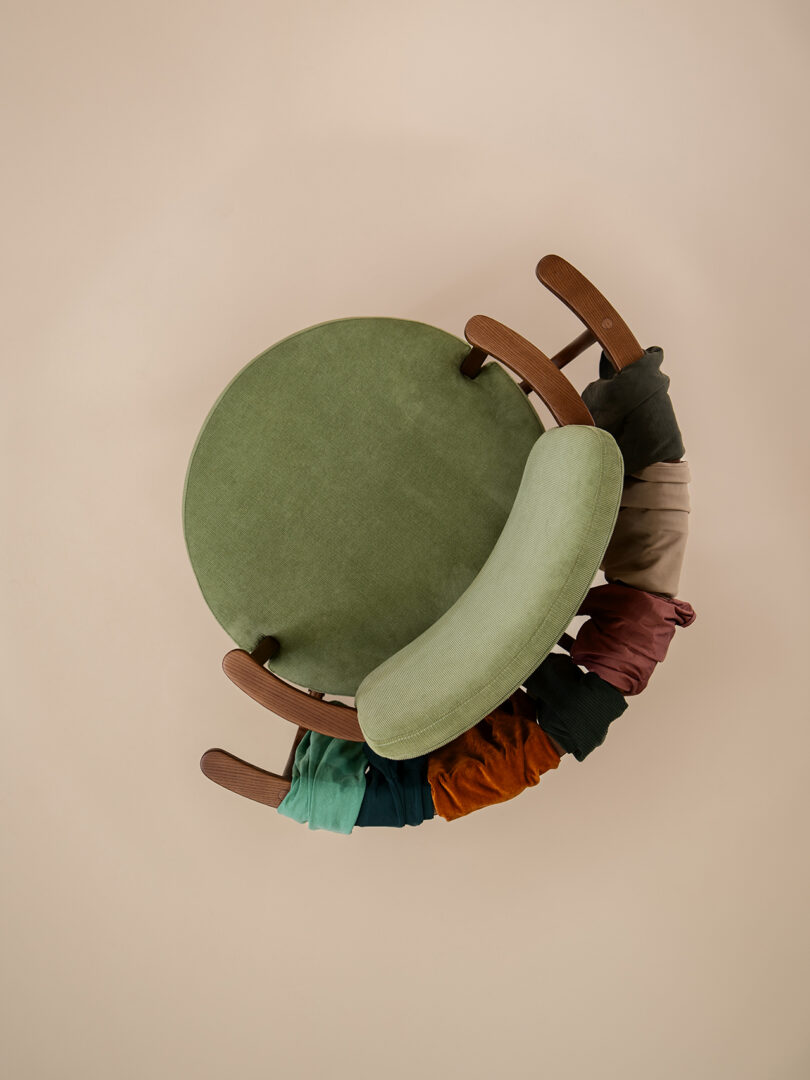 A green upholstered chair with wooden arms, viewed from above, with various colorful fabric pieces draped over the front edge of the seat.