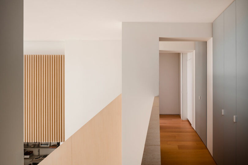 Modern interior hallway with wooden floor, light-colored walls, vertical wood slats on the left, and built-in storage cabinets on the right.