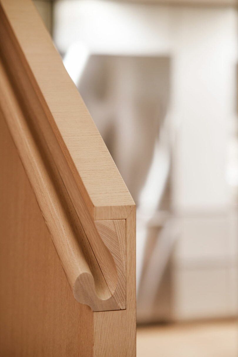 Close-up of a wooden handrail on a staircase with a blurred background showing a modern, light-filled interior.