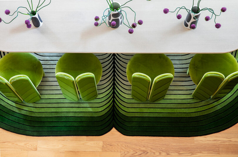 Overhead view of a white table with three green chairs and a green striped rug, decorated with vases containing purple flowers.