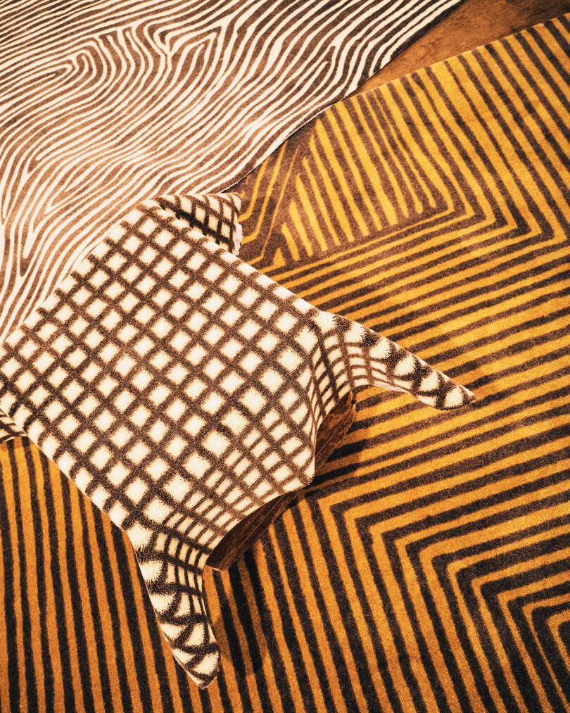 Overhead view of three patterned rugs overlapping: one with zebra stripes, one with a grid pattern, and one with yellow and brown geometric stripes.