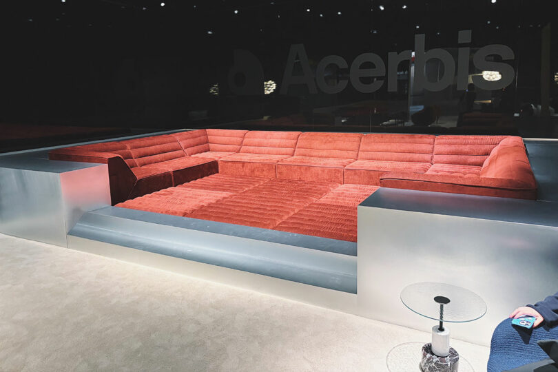 Sunken red sectional sofa with ribbed upholstery, surrounded by metallic framing, set in a modern showroom with 