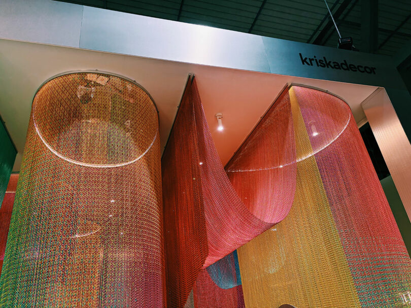 Colorful metal chain curtains in red, yellow, and orange hang from the ceiling at a display booth labeled 