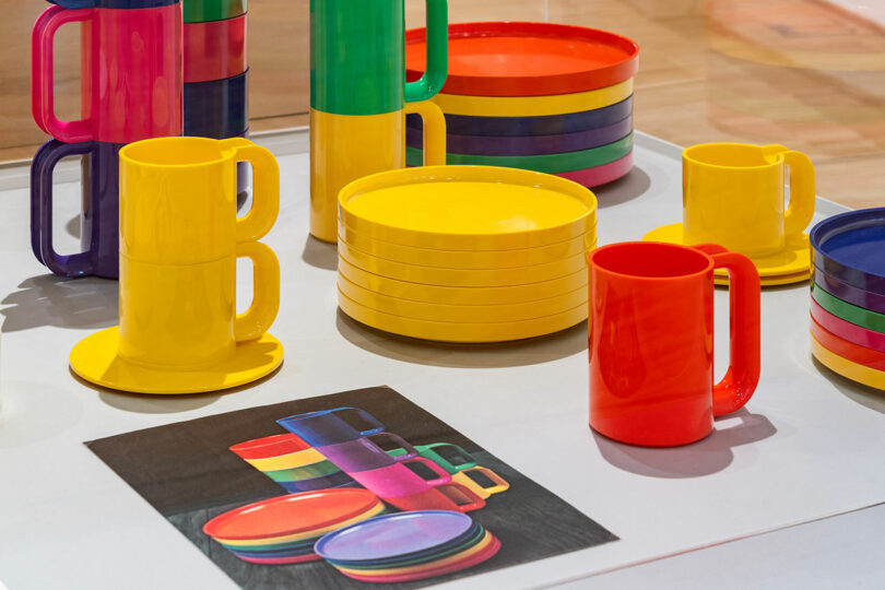 Colorful plastic cups, bowls, and plates with large handles are displayed on a white surface next to an illustration of the same items.